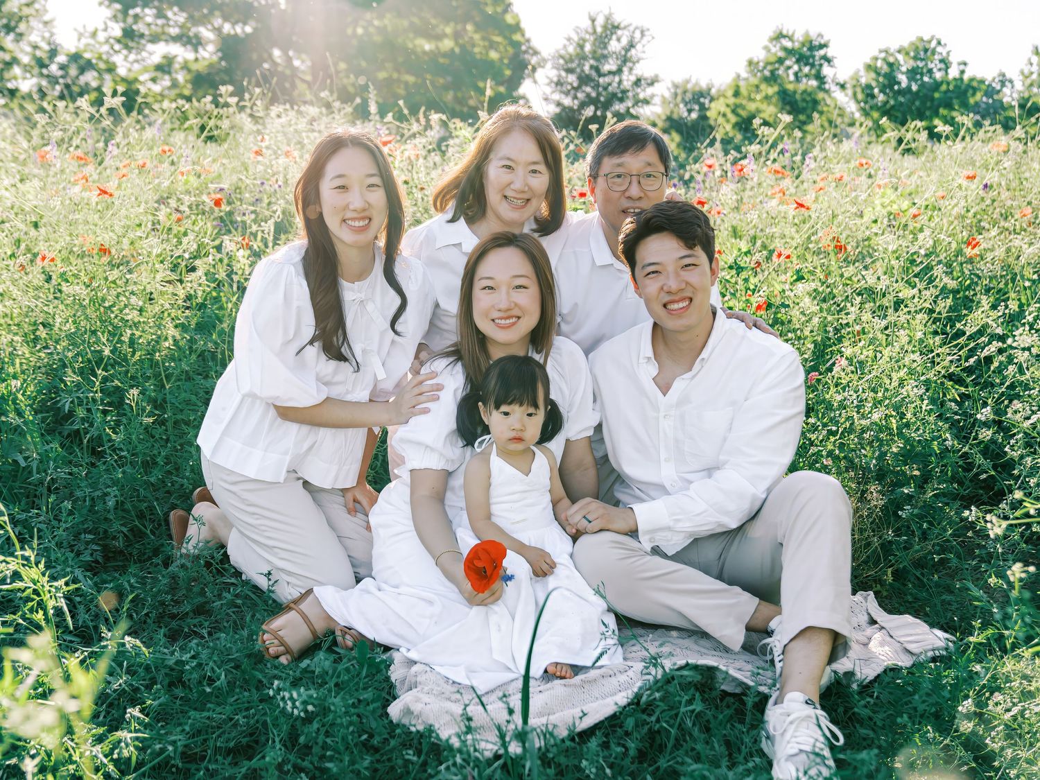 Family wearing white outfits poses together in a blooming flower field on a sunny day.