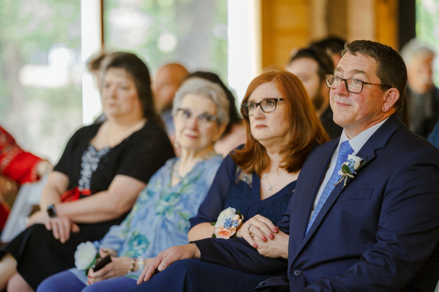Wedding guests seated in rows at an outdoor ceremony venue with natural greenery and trees in the background.