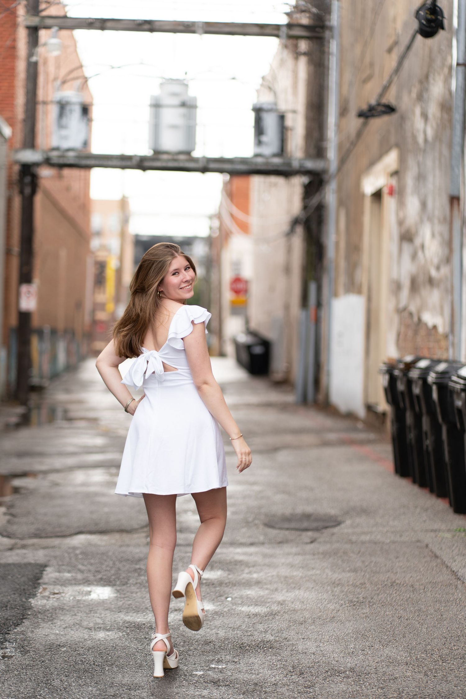 A series of photos showing a person in a white dress running down an urban alley with brick buildings and trash bins.