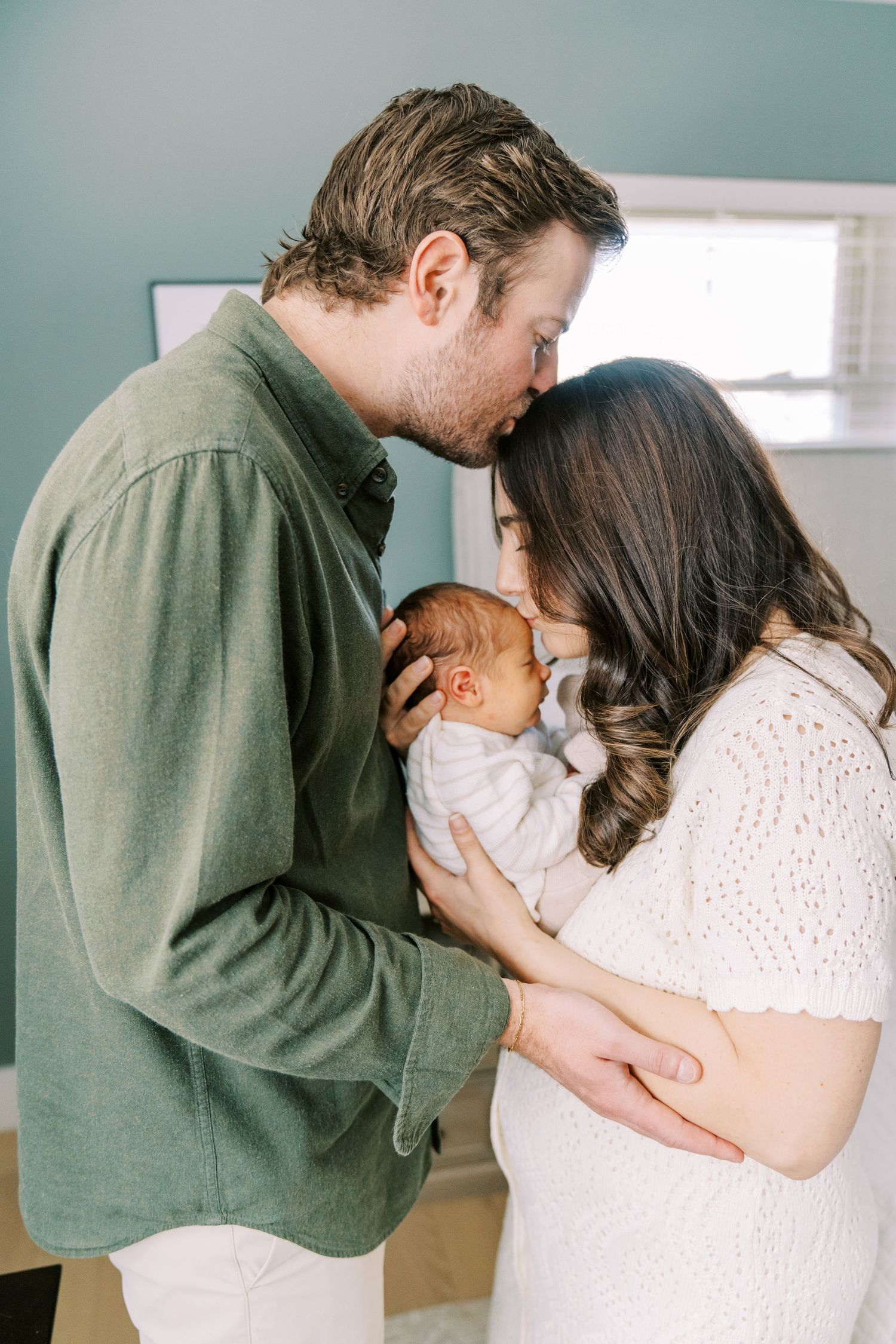 A tender family moment in a nursery as parents share an intimate embrace with their newborn baby.