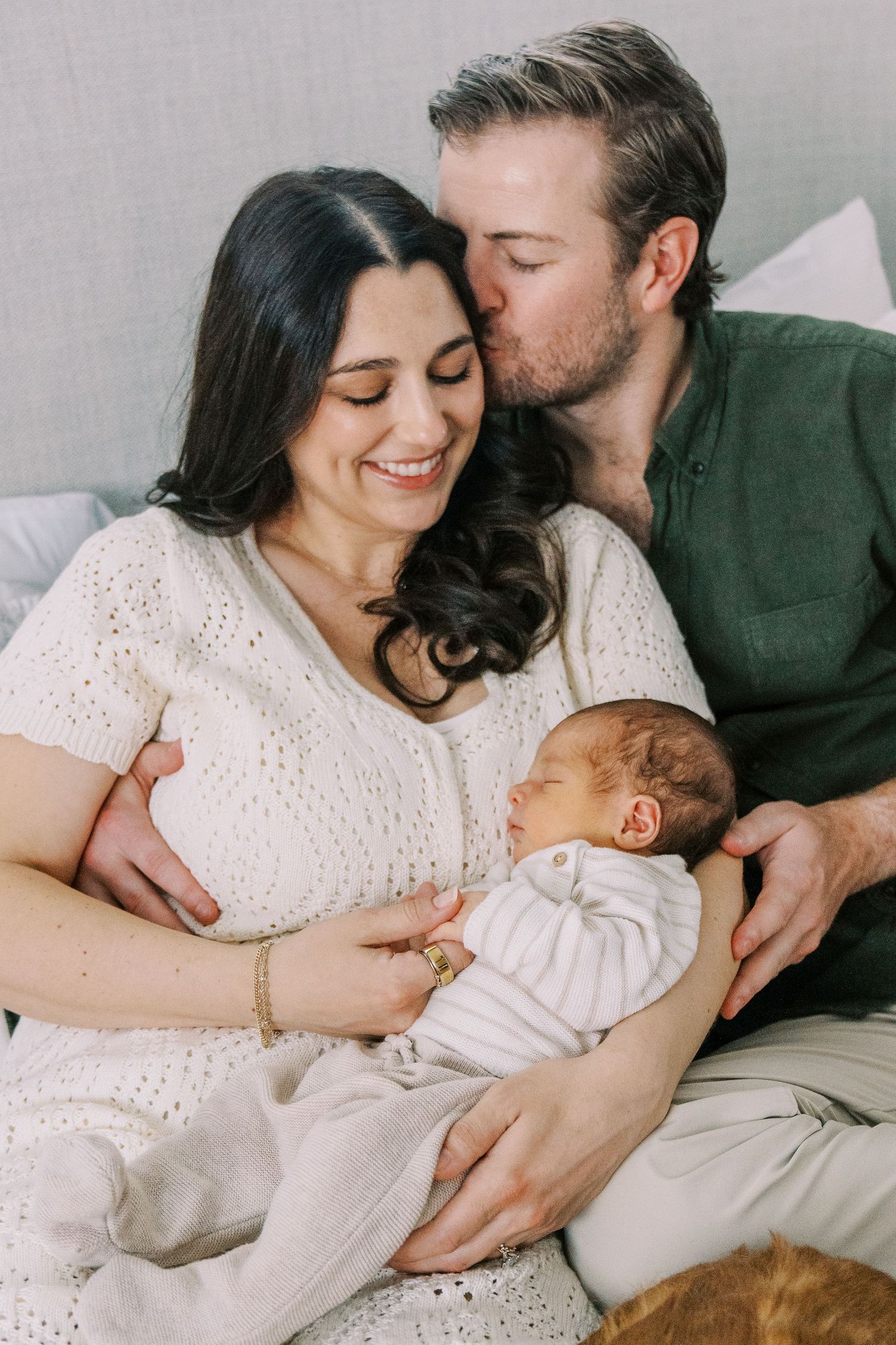Intimate lifestyle photos of family lying together on white bedding showing tender moments and embraces.