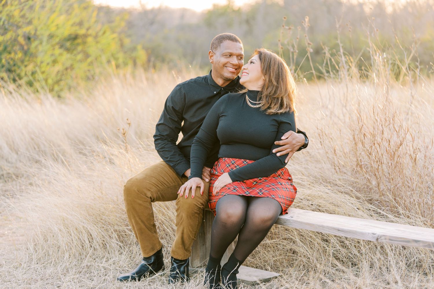 Couple sitting together in golden sunlit field during autumn sunset photoshoot.