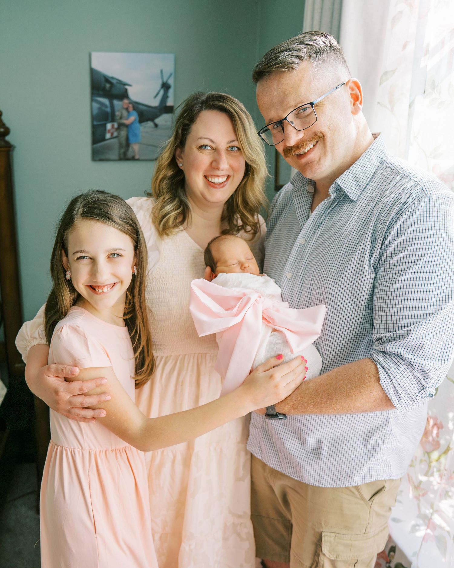 A family shares tender moments in matching pink and grey outfits by a window with natural light.