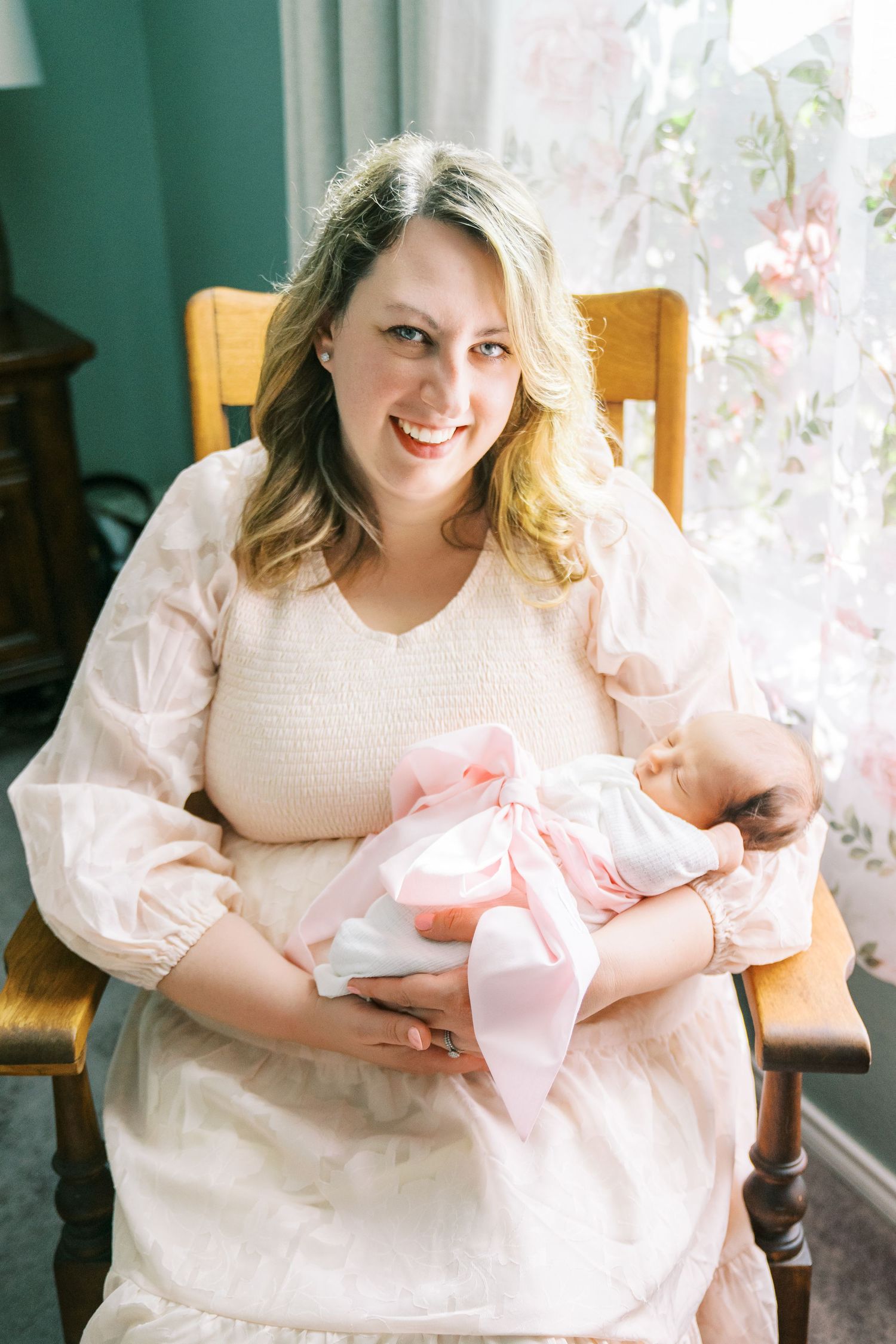 A peaceful moment in a wooden rocking chair as mother holds sleeping newborn in pink blanket.
