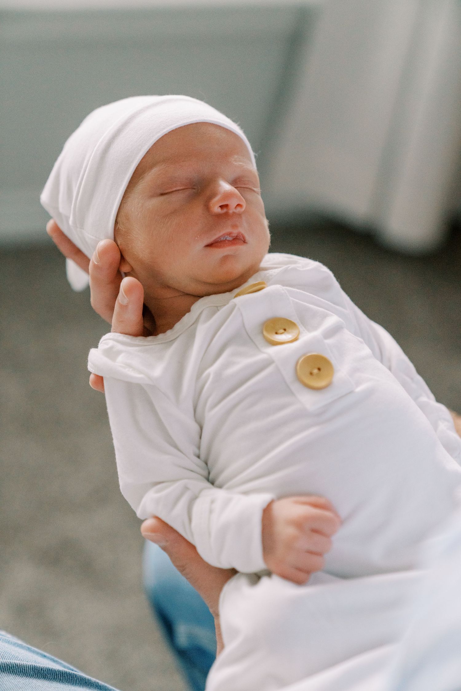 Sleeping newborn baby wearing white outfit with decorative buttons.