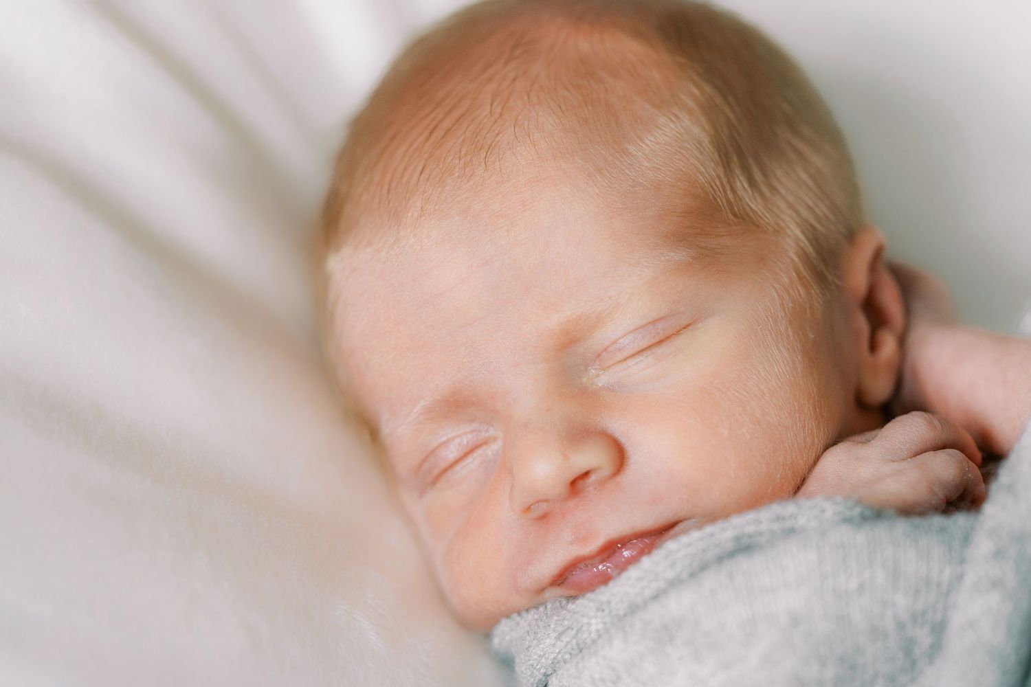 Sleeping newborn baby wrapped in soft gray blanket resting peacefully on white bedding.