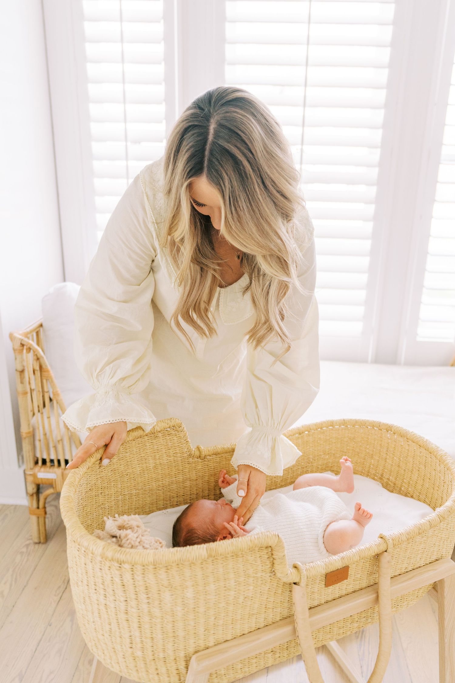 Baby rests peacefully in woven bassinet while parent watches from above in bright room.