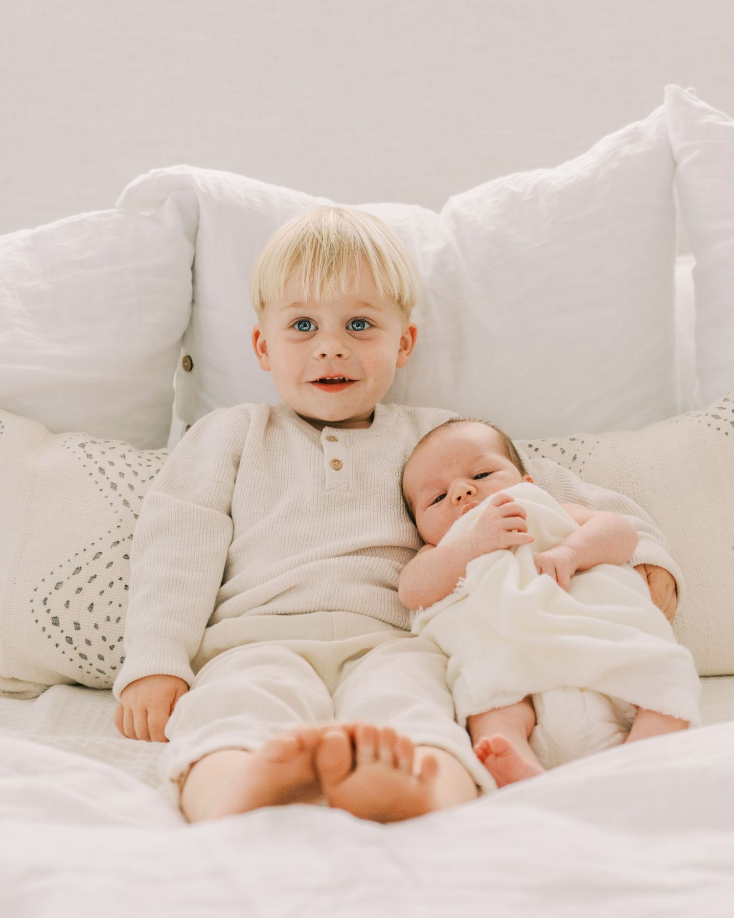 Two young children in white clothing playing together on a cozy bed.