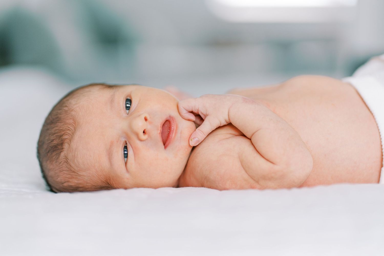 Adorable newborn baby lying on soft white blanket in gentle natural light.