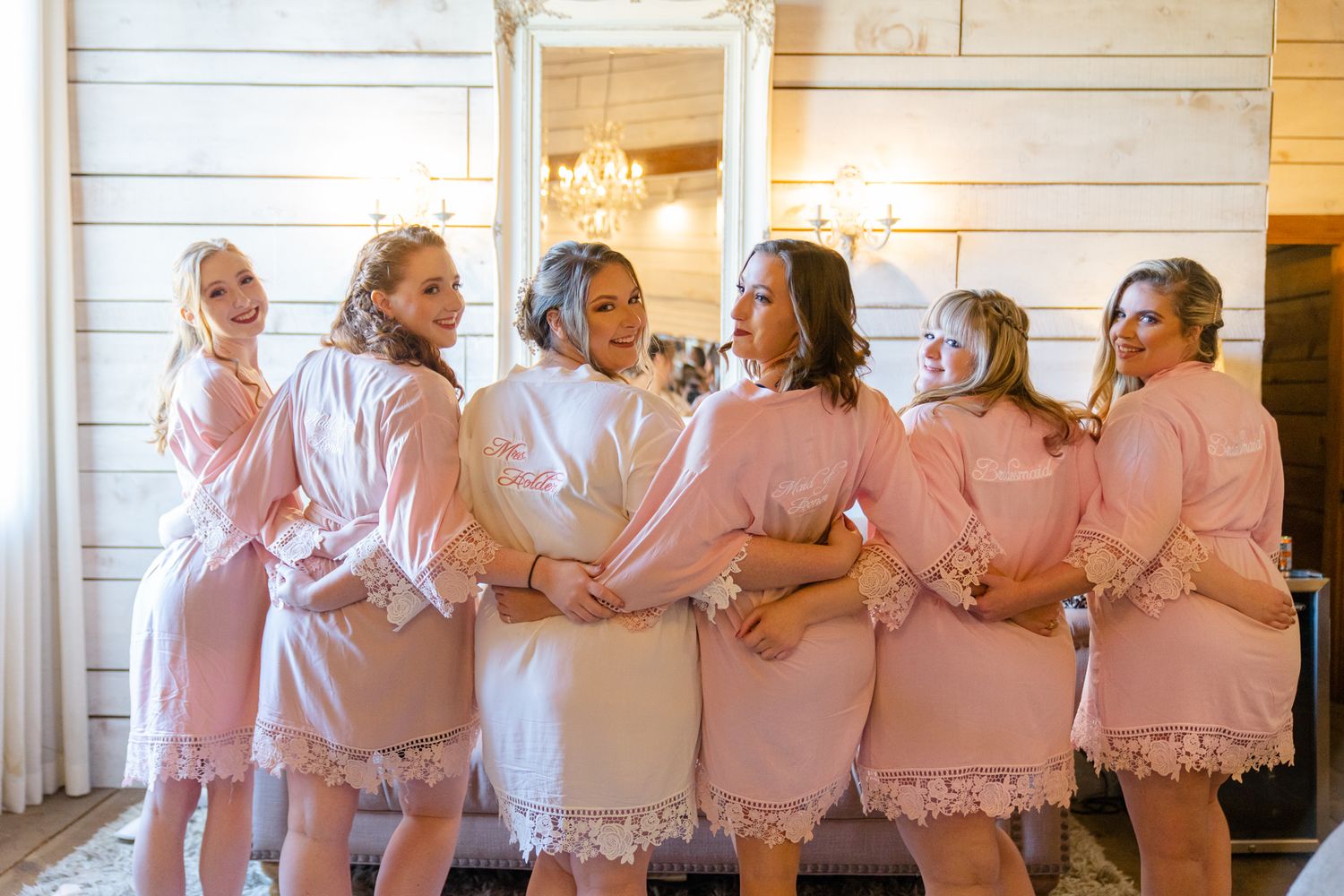 Group wearing matching pink robes gather together in a rustic white wood-paneled room.