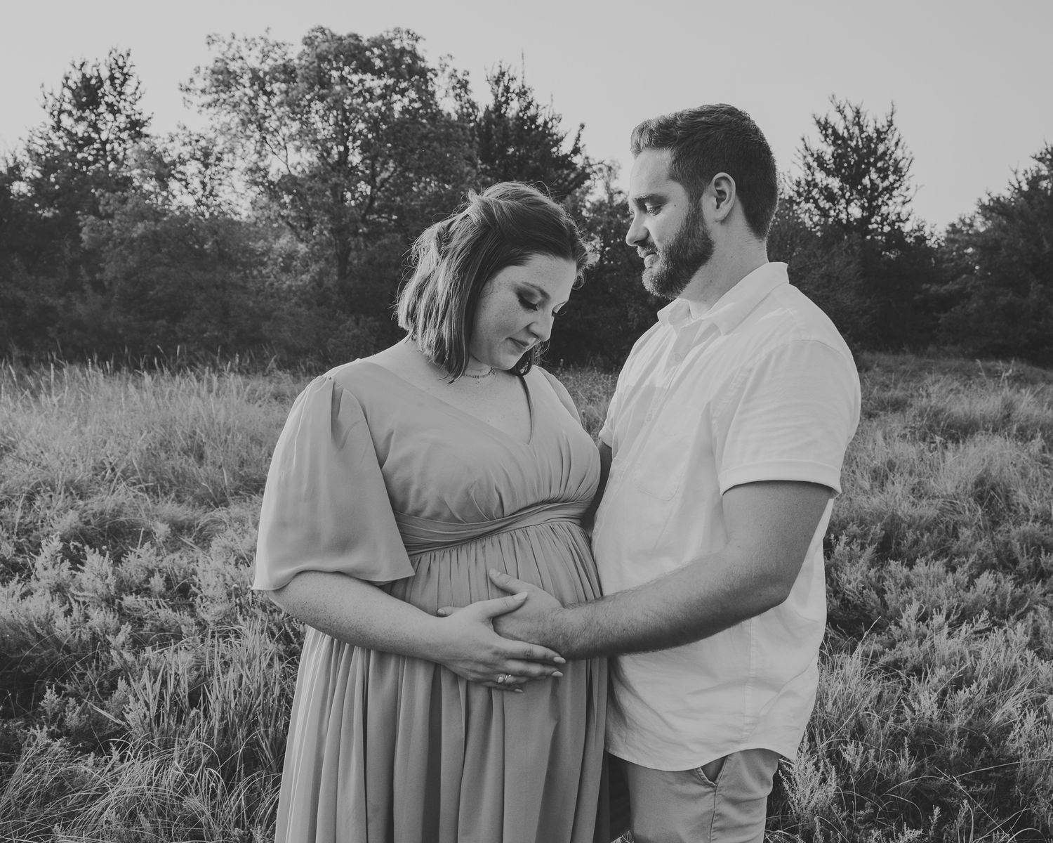 A romantic black and white photo series of a couple embracing in a meadow during an outdoor photography session.