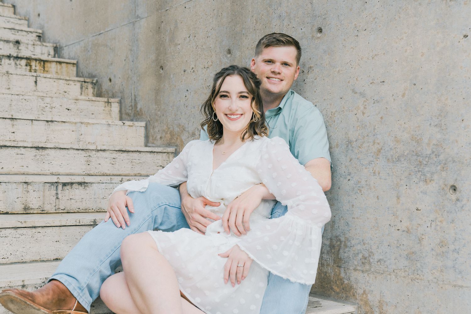 Couple sharing intimate moments on outdoor concrete steps in soft lighting.
