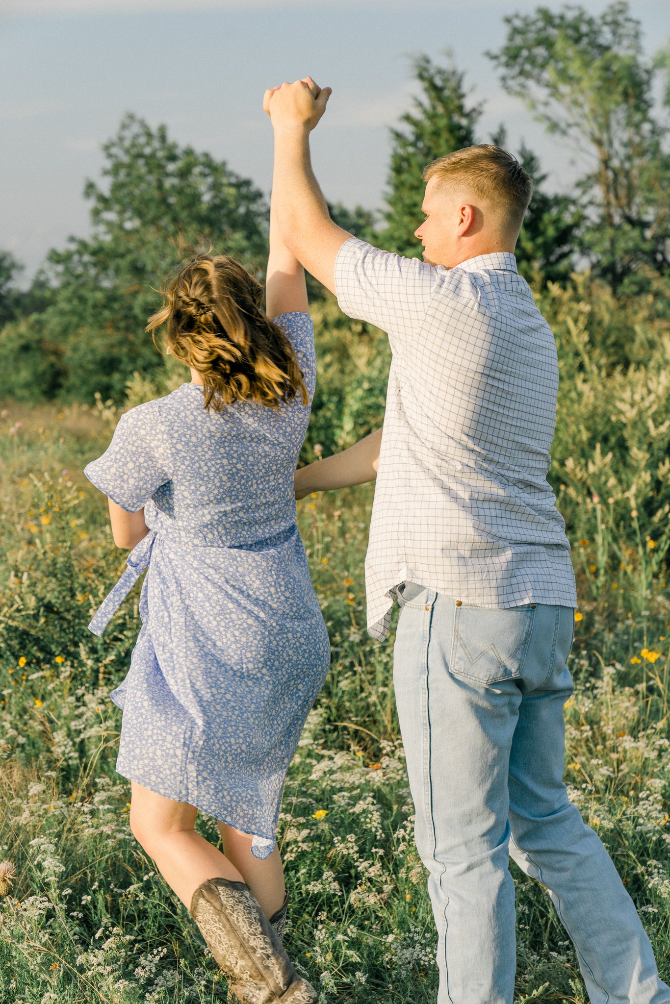 Couple dancing and jumping joyfully in a wildflower meadow wearing casual summer clothes.