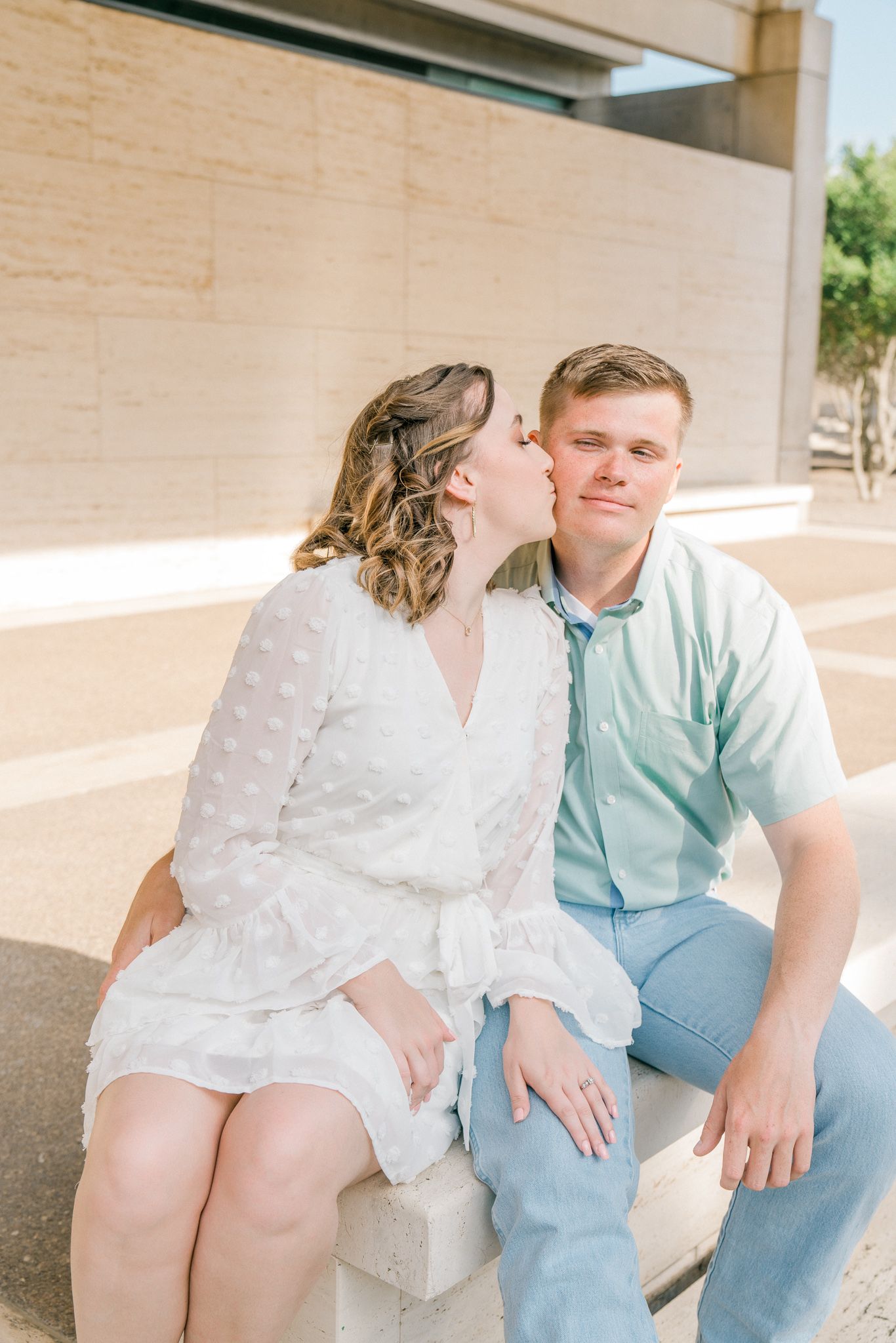 A couple in white and blue outfits share romantic moments in a series of engagement photos against a light-colored wall.