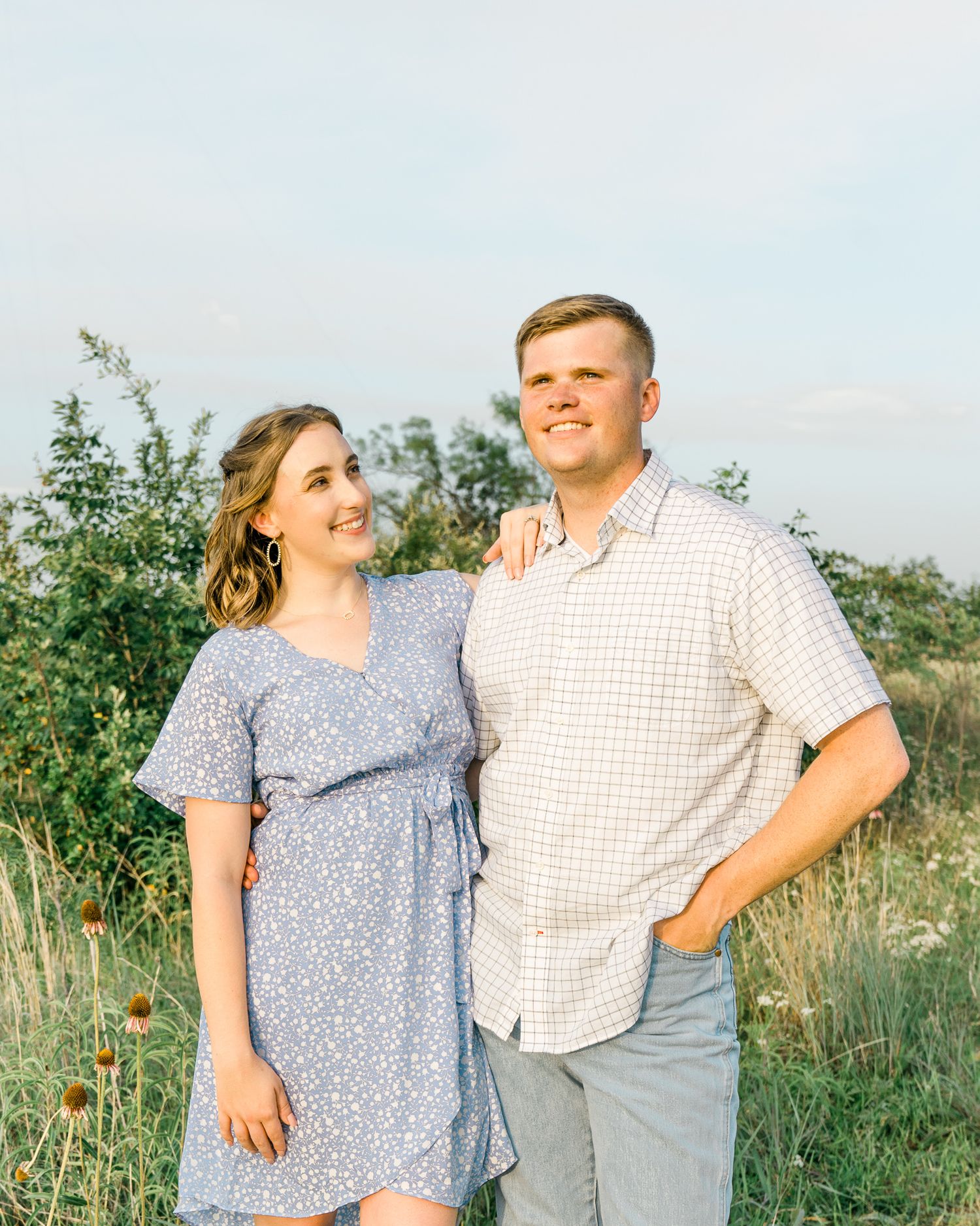 A couple poses together in a wildflower field during golden hour wearing casual summer attire.