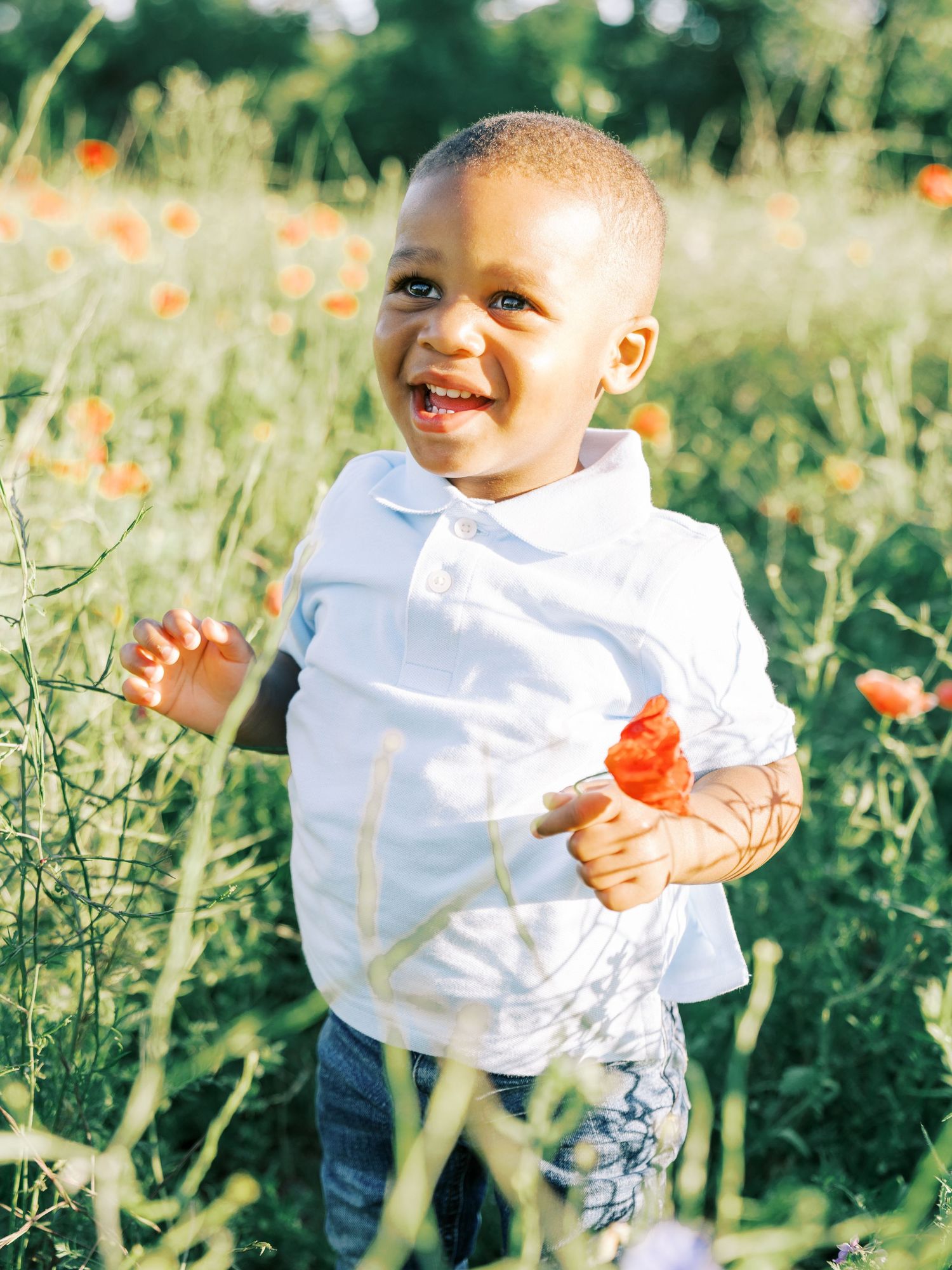A joyful child plays in a wildflower meadow wearing a white shirt and blue pants on a sunny day.