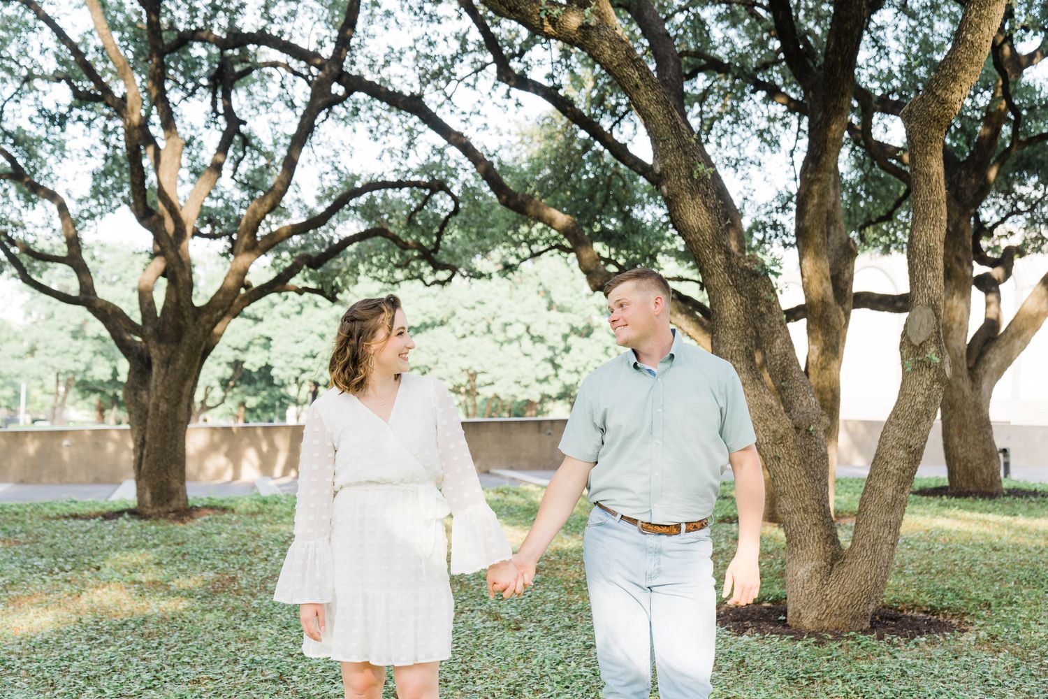 Couple walks together holding hands under a canopy of trees in a romantic outdoor setting.