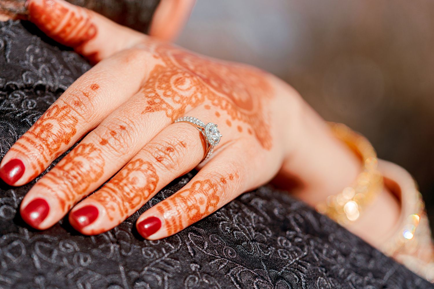 Close-up of hands with red nail polish and intricate henna designs creating traditional mehndi art patterns.