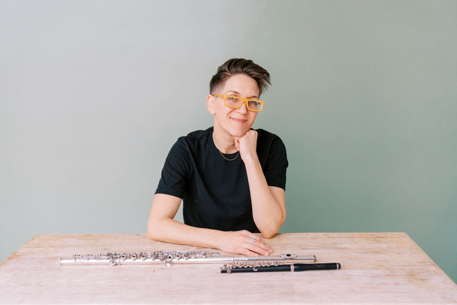 A person in a black t-shirt sits at a wooden table with a clarinet in front of them.