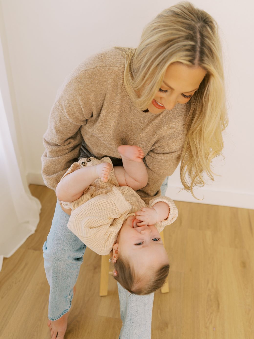 Parent and child sharing playful interactions while sitting on wooden furniture in a minimalist setting.