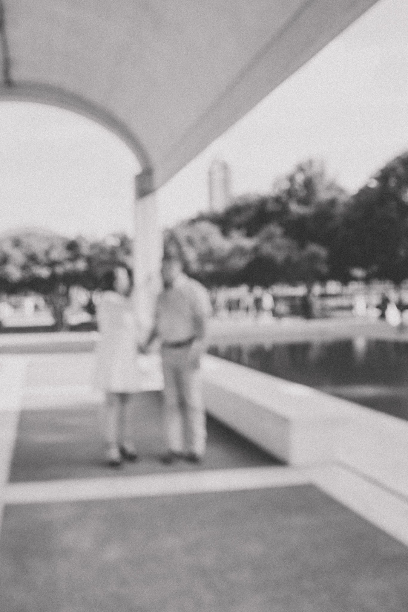 Couple walking along a covered outdoor walkway with white columns and greenery in the background.