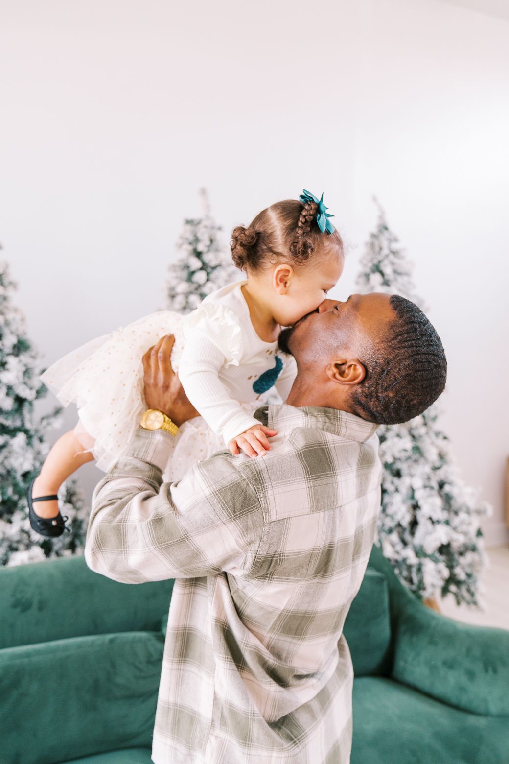 Sweet candid moments captured during a holiday photoshoot with snowy Christmas trees in the background.