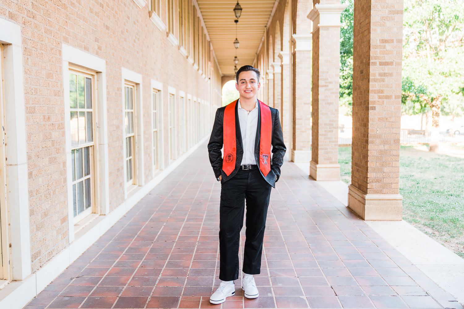 A person in a red jacket walks along a brick-lined covered walkway at a university campus.
