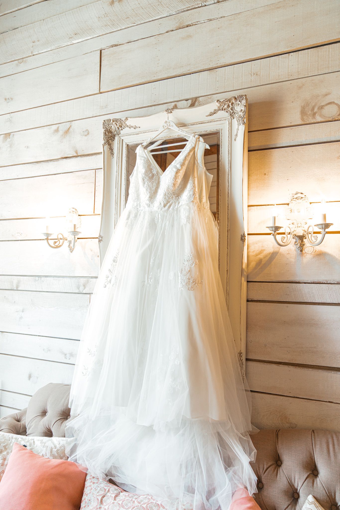 White wedding dresses displayed against rustic wooden wall with elegant wall sconces.