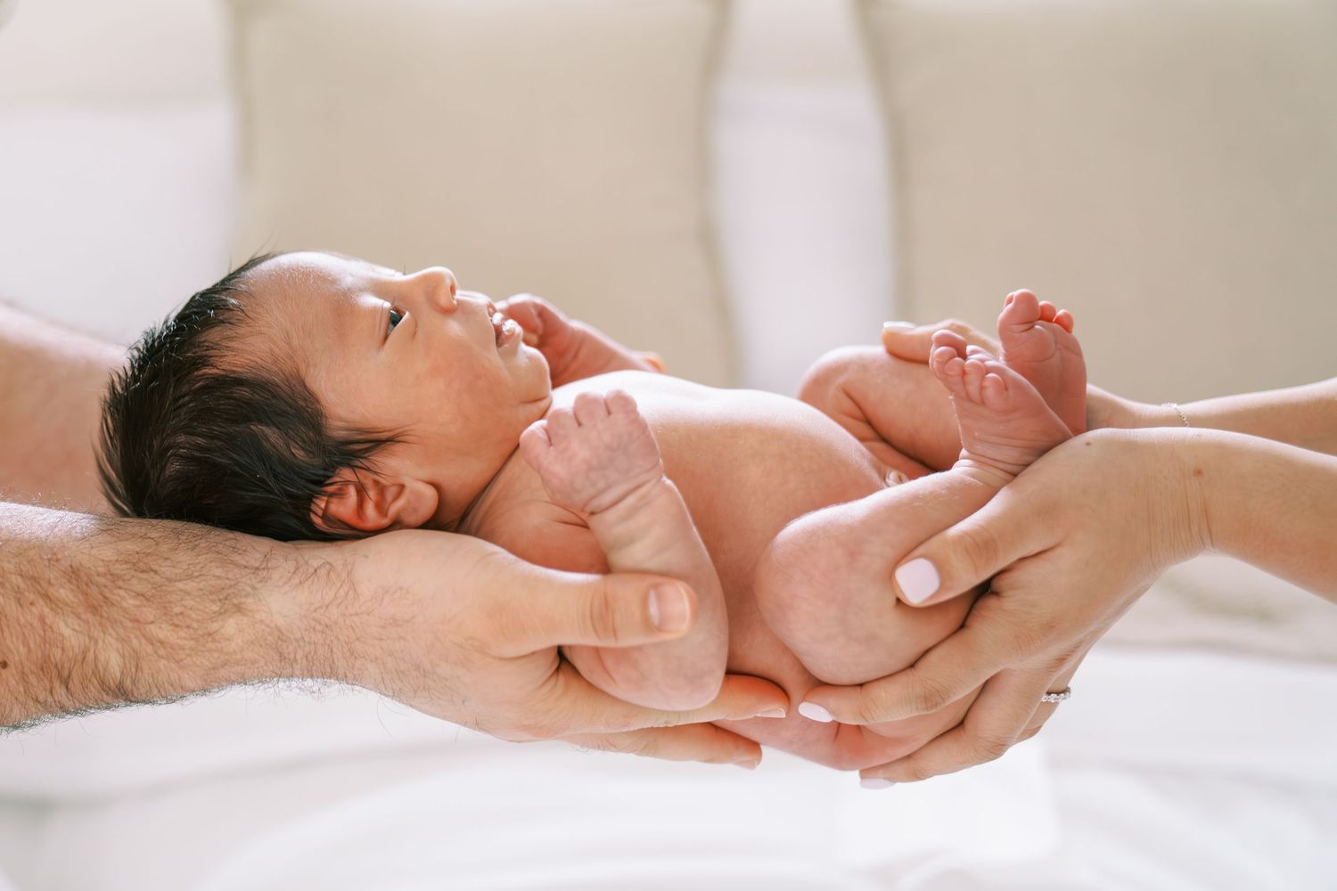 Newborn baby cradled gently in parents hands, lying on a soft white blanket in a serene setting.