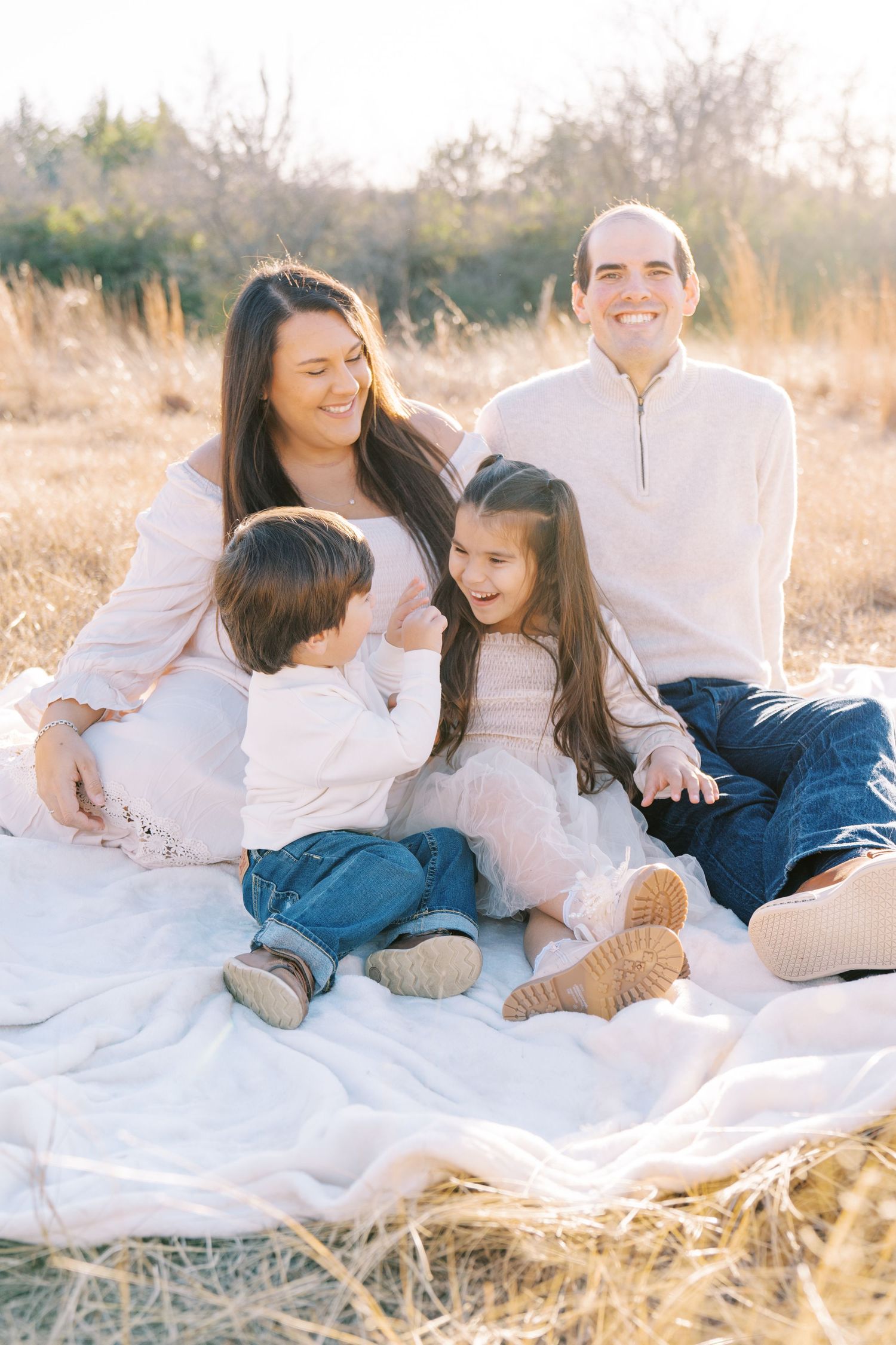 A family lounges together on a white blanket in a sun-drenched field during golden hour.