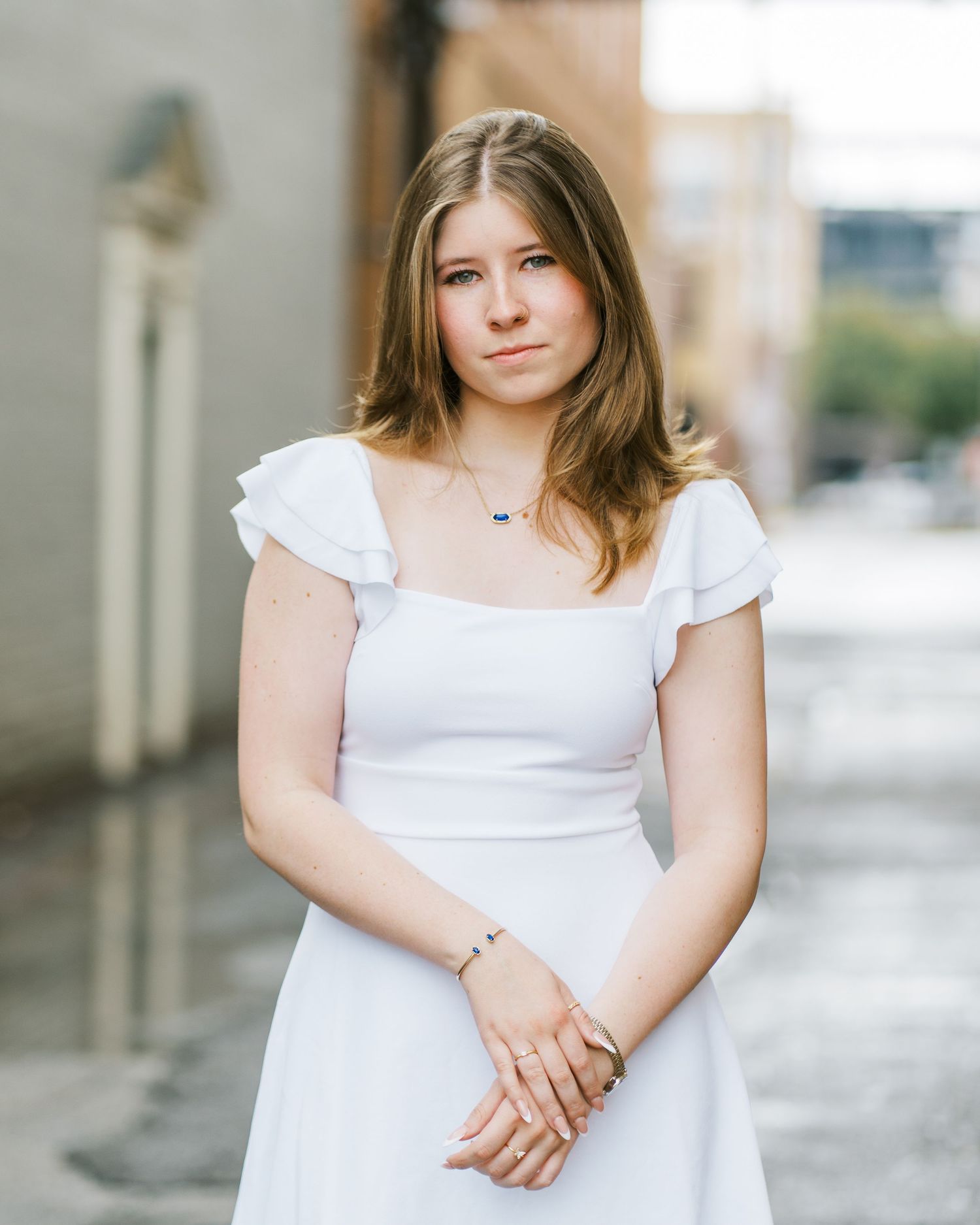 A person in a white summer dress poses outdoors against a blurred urban background.