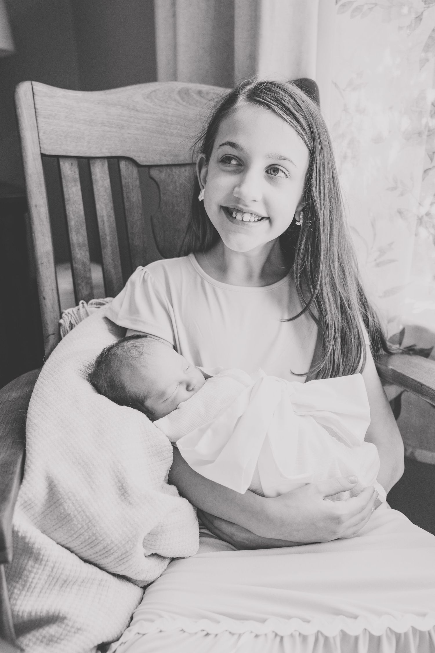 A heartwarming moment captured in black and white as a young girl holds a sleeping newborn.