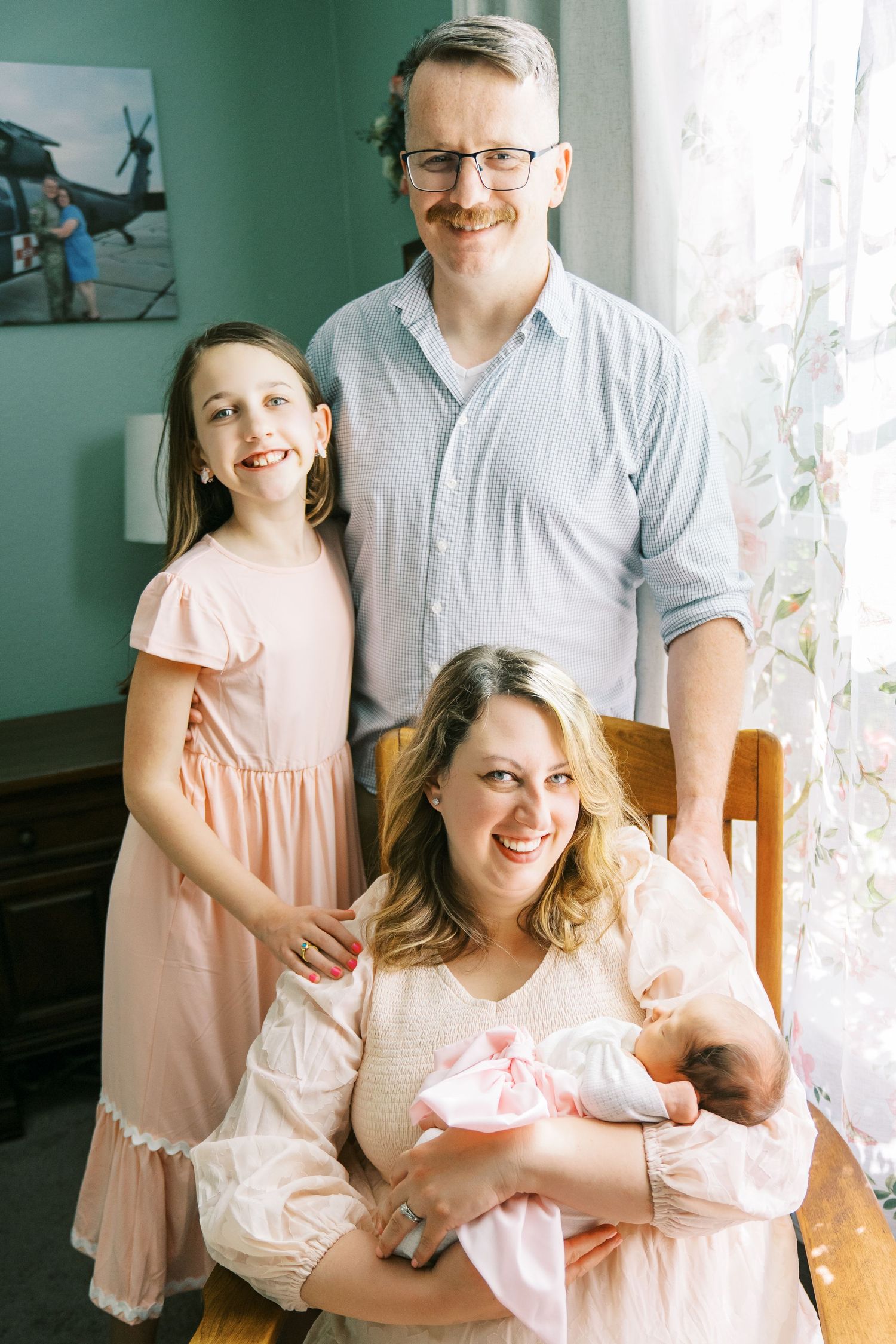 Family portrait session in mint green room with matching pink outfits and natural window light.