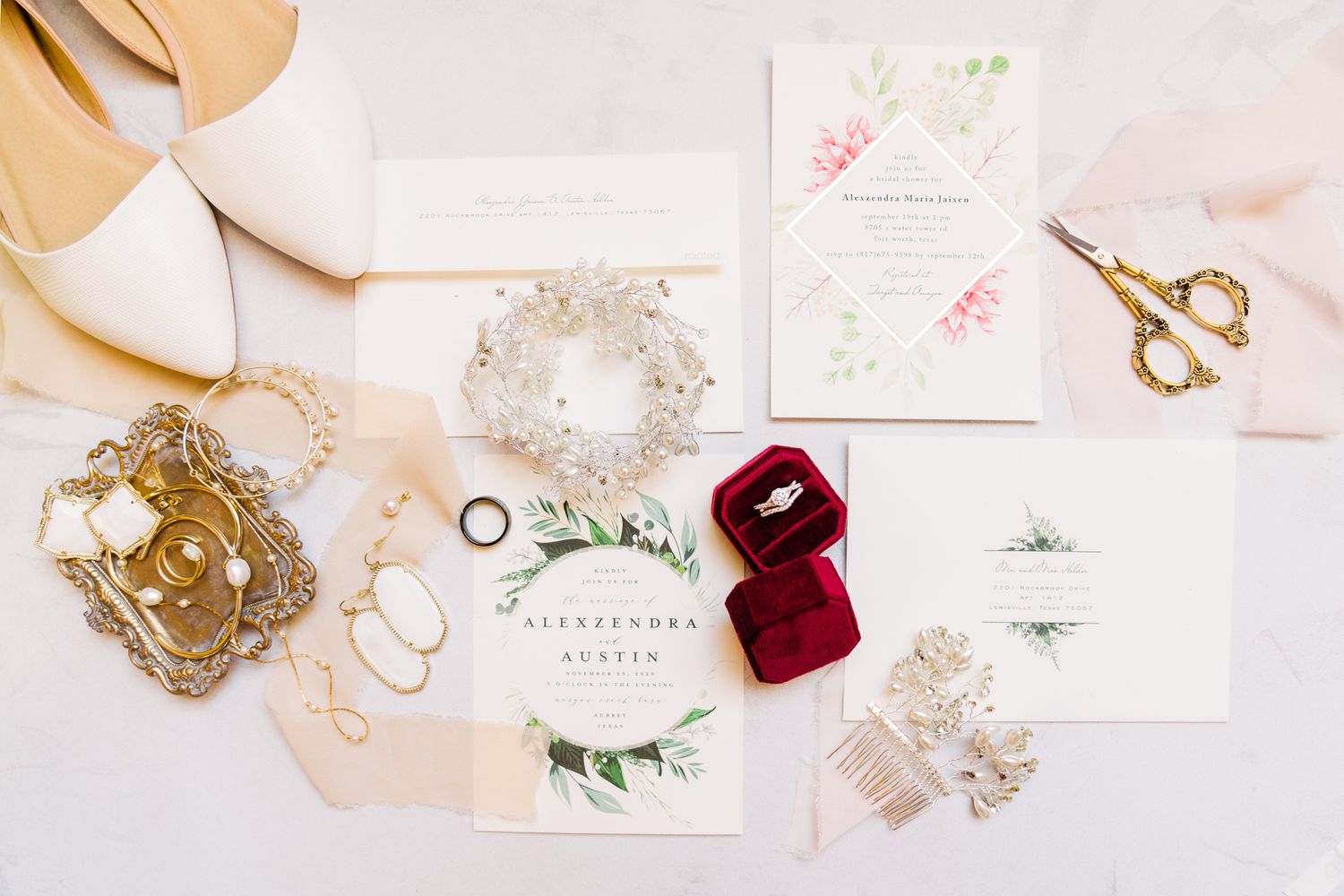 Wedding invitation suite with gold jewelry, velvet ring box, and delicate floral details on a light pink background.