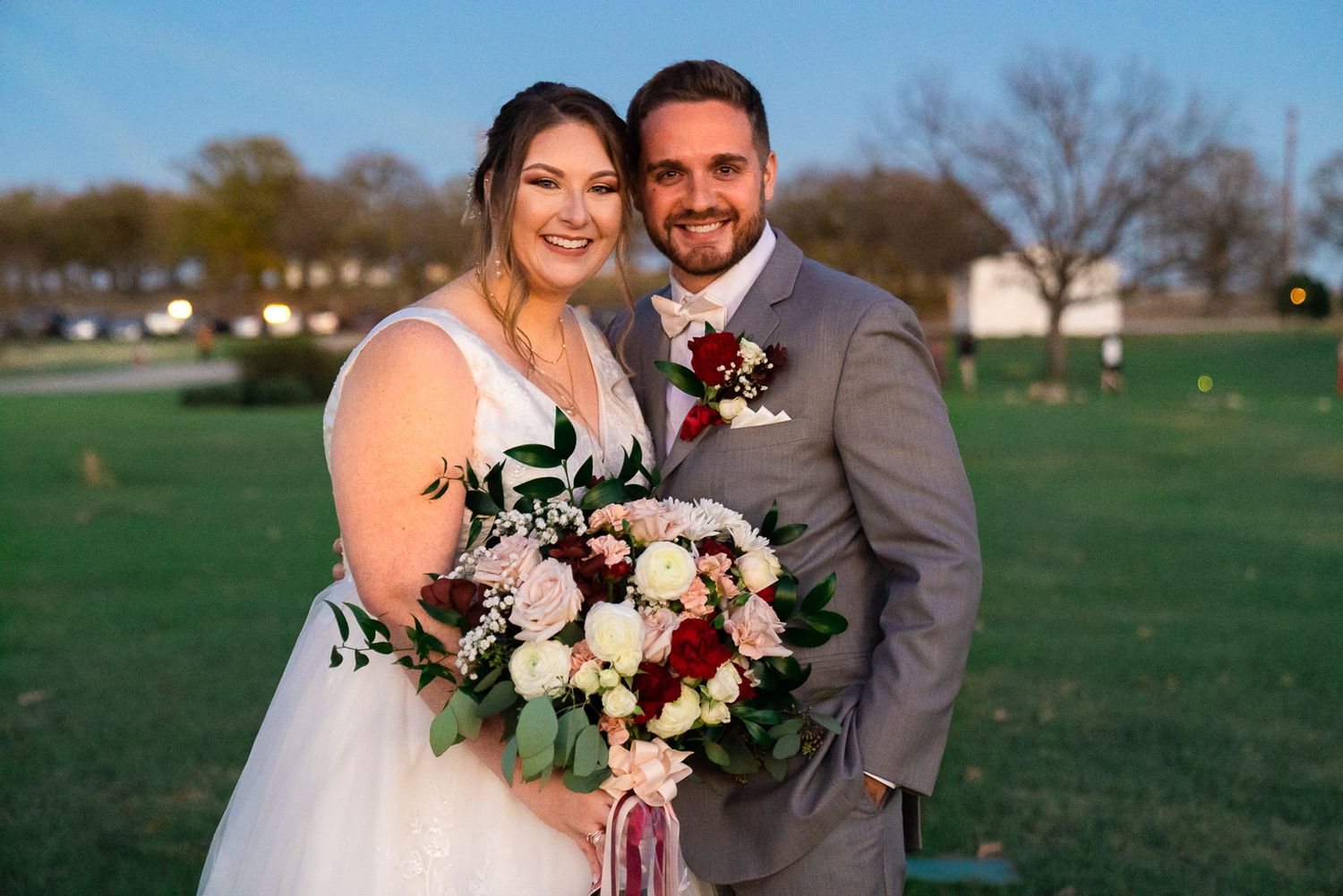 Wedding couple stands together on a green lawn during an outdoor autumn ceremony.