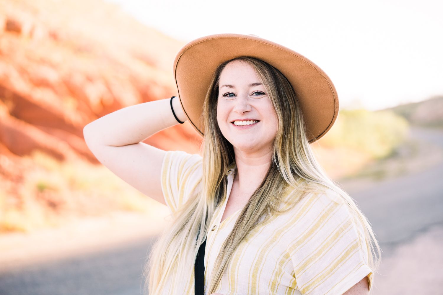 Candid portrait of someone wearing a brown hat and white top against desert rock formations.