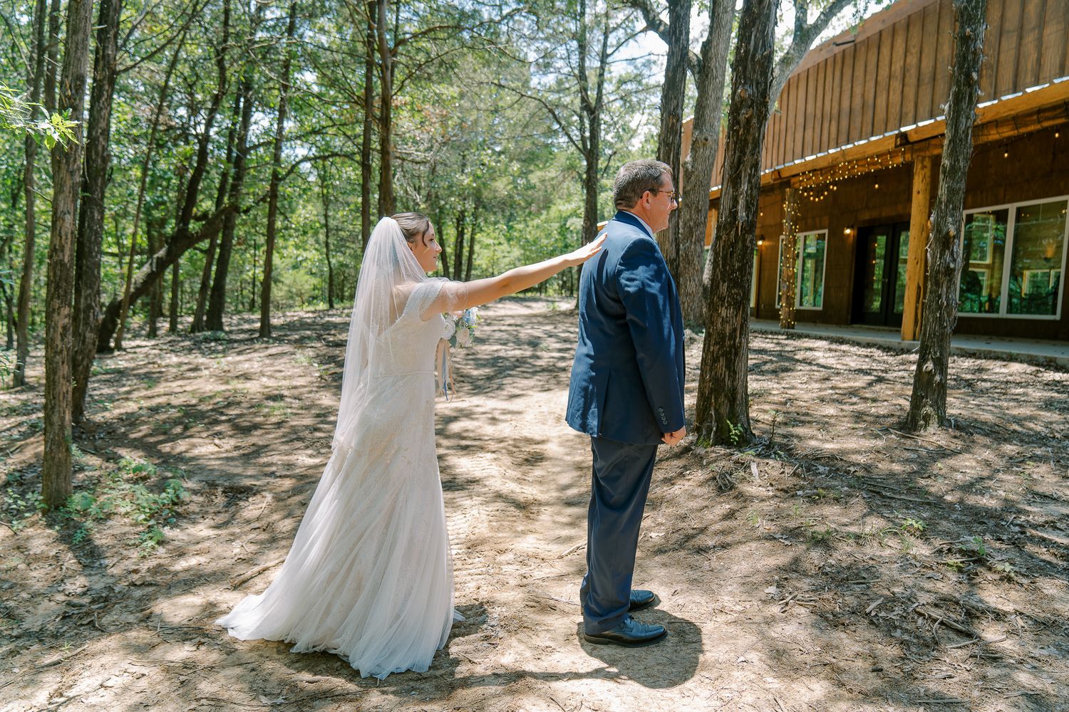 A couple shares a romantic moment during their outdoor forest wedding ceremony on a wooded path.