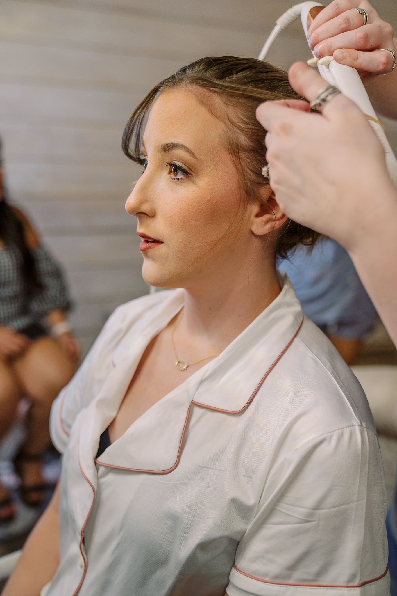 A stylist uses a hair tool on a client wearing a white robe during a beauty preparation session.