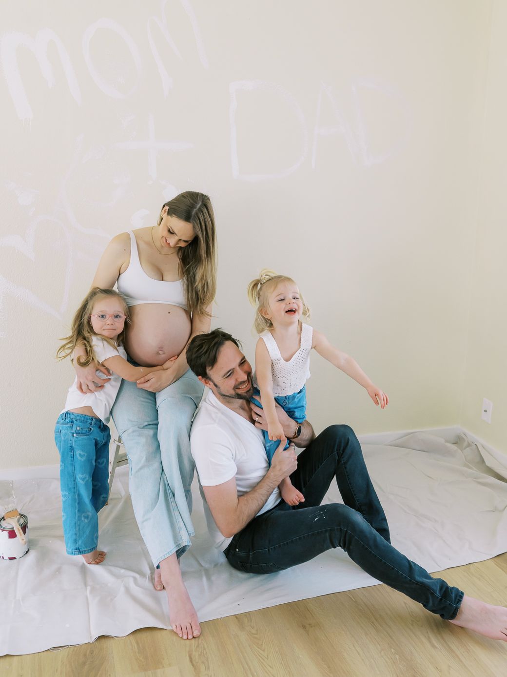 Joyful family moment during maternity photoshoot on white backdrop.