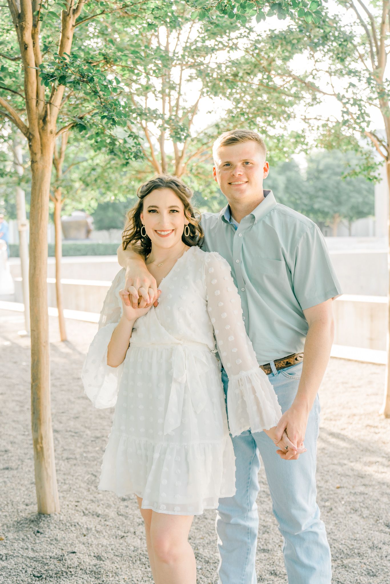 Joyful couple laughing together during outdoor photoshoot among trees.