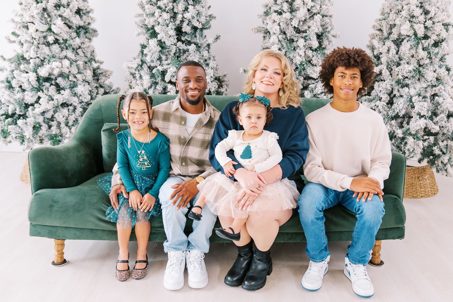 Family holiday portrait session in front of snow-flocked Christmas trees with woven baskets.