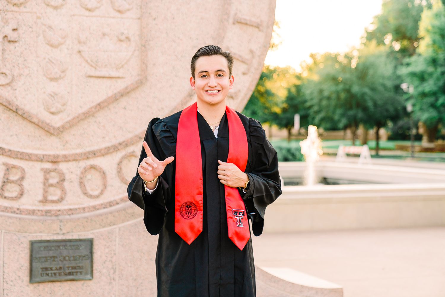 Graduate in black academic regalia and red stole celebrates with enthusiasm during outdoor commencement ceremony.