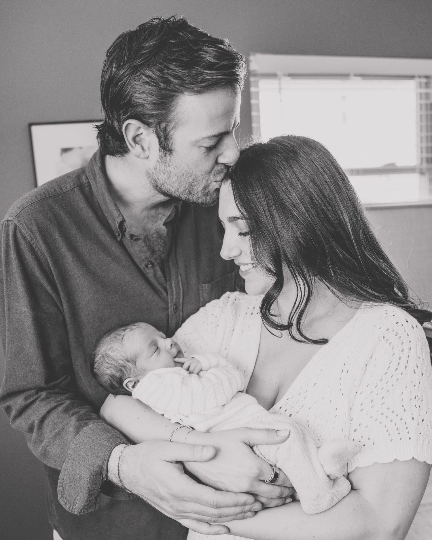 A tender black and white photo series showing intimate family moments with a newborn baby and parents sharing loving embraces.