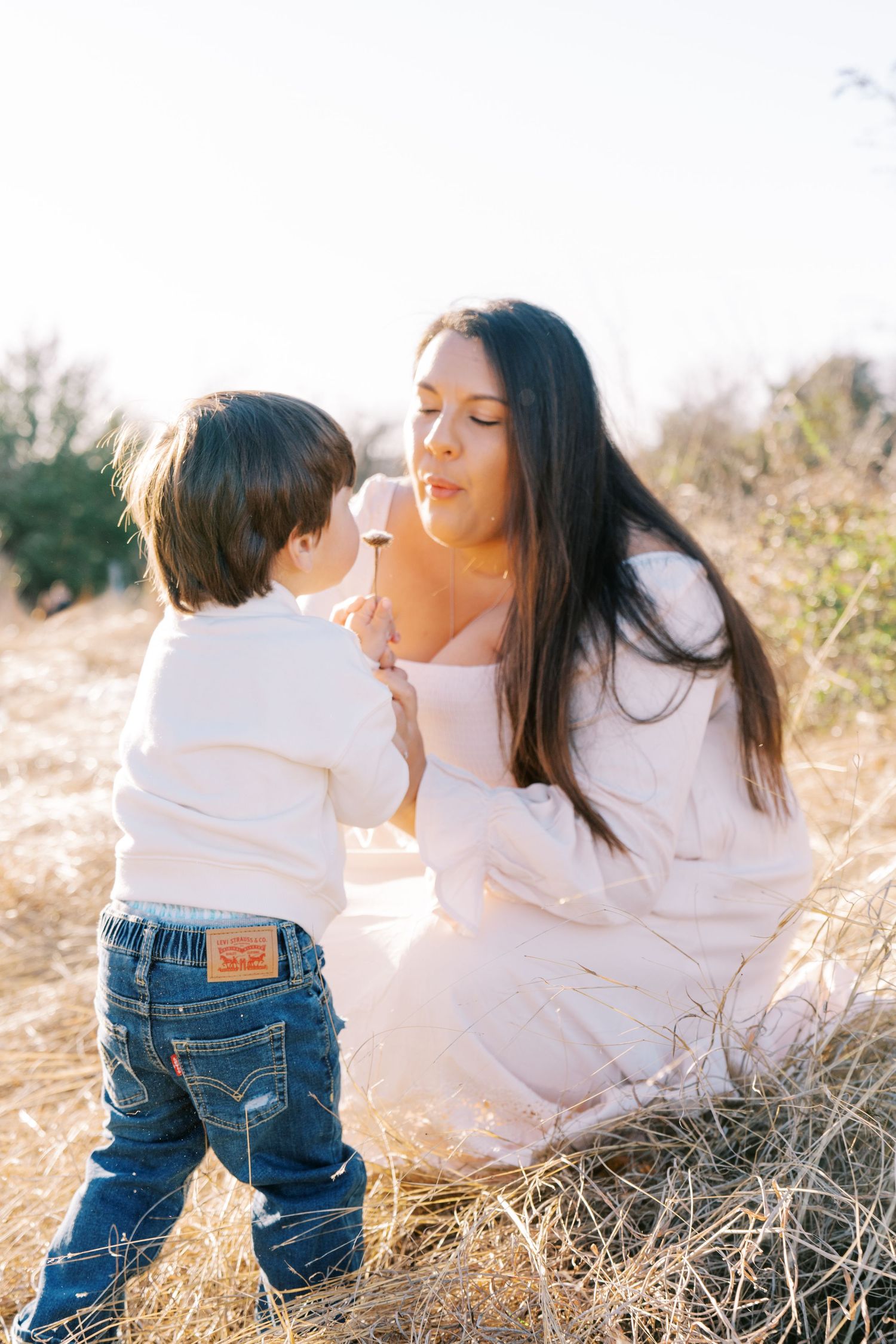 Parent and child share tender moments in a sun-drenched field while wearing white shirts and jeans.