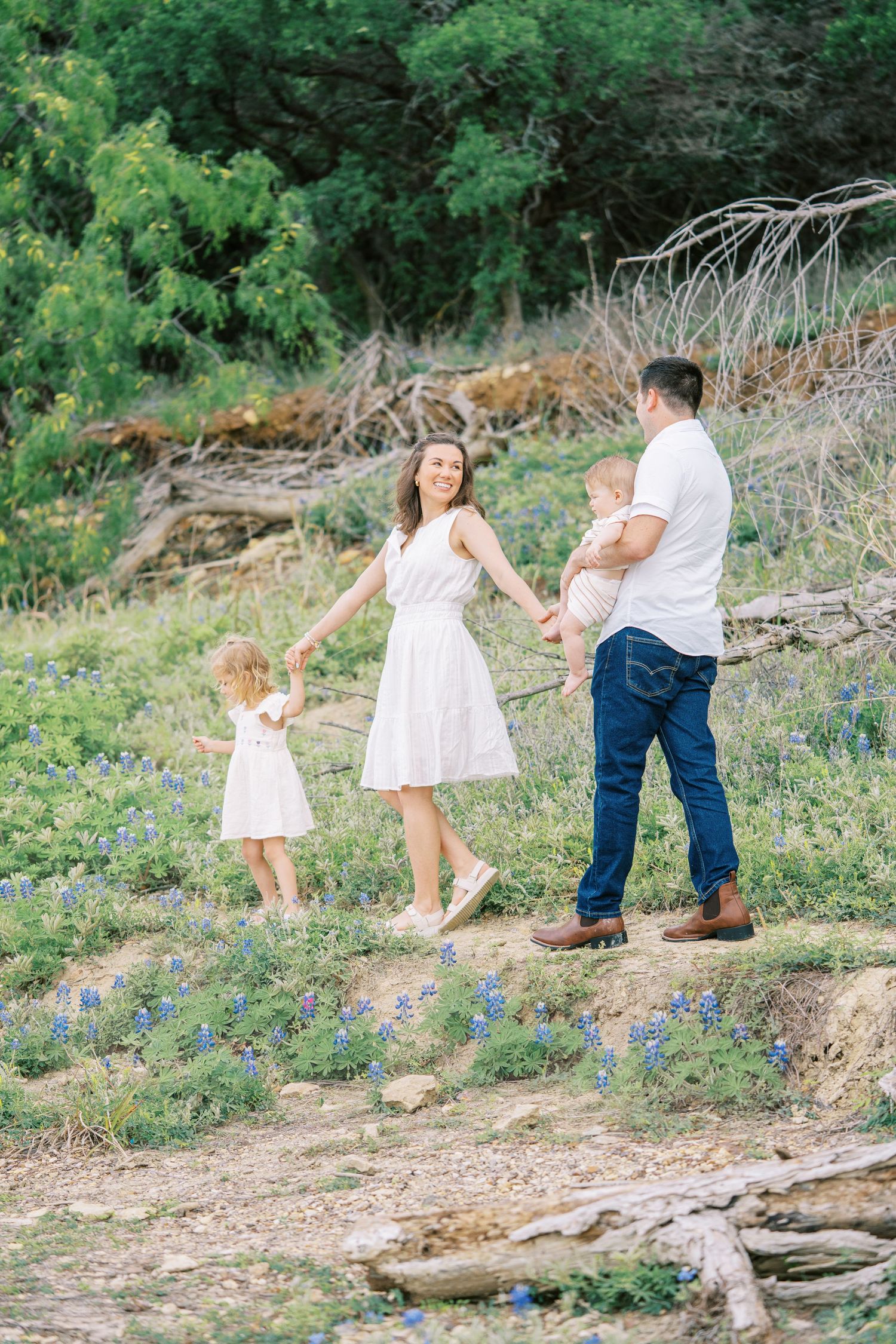 Family of four enjoying bluebonnets in Texas, parents holding children while walking through wildflower field.