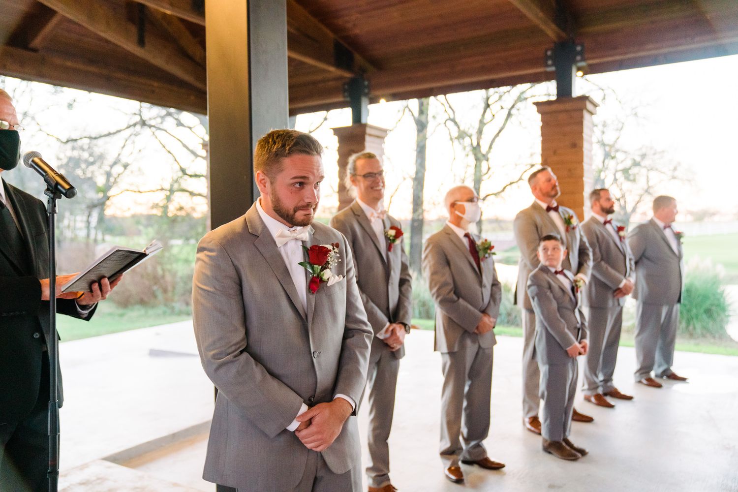 Groomsmen in matching gray suits stand in line during a wedding ceremony.