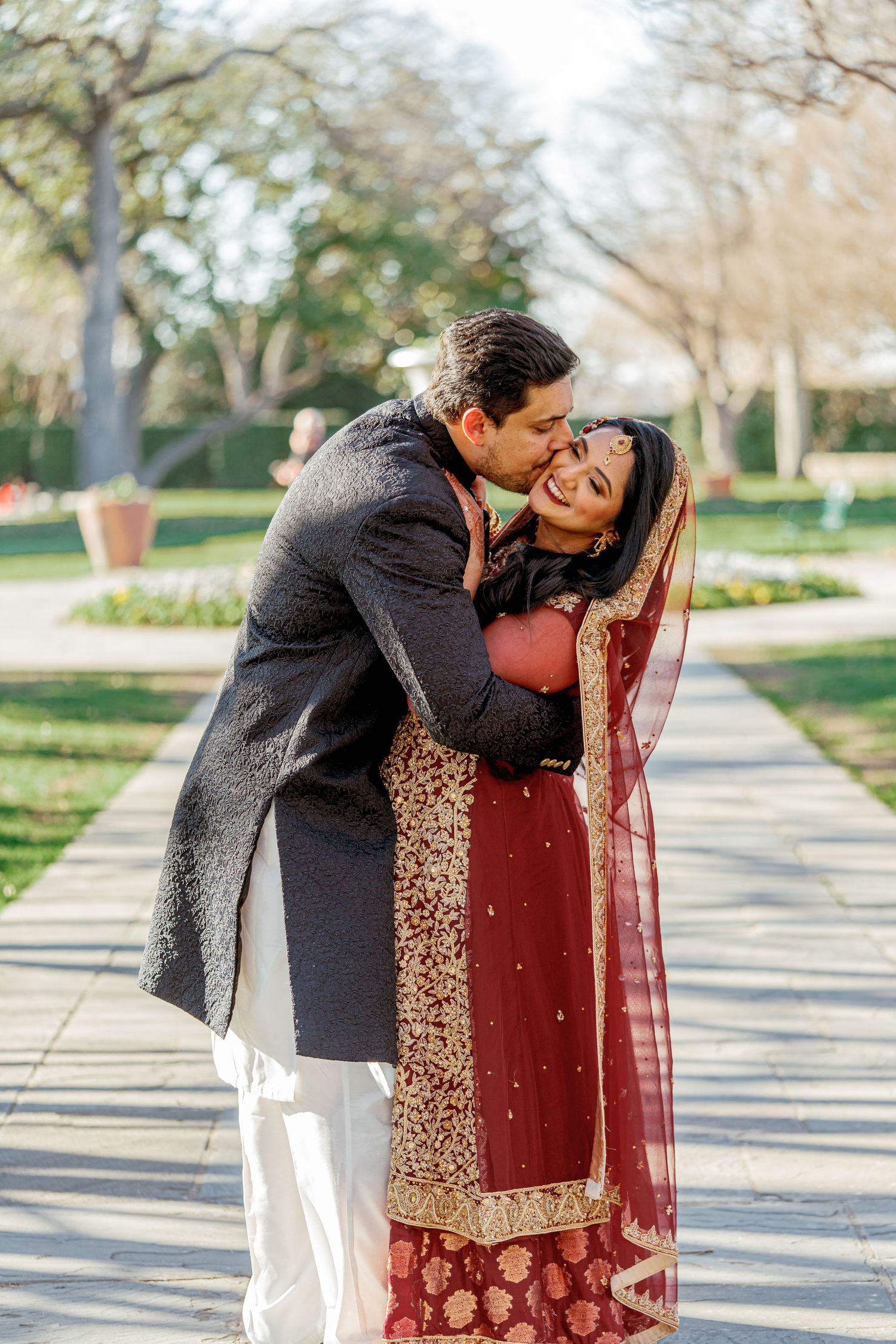 A romantic outdoor photoshoot showing a couple in traditional South Asian attire sharing tender moments in a park setting.