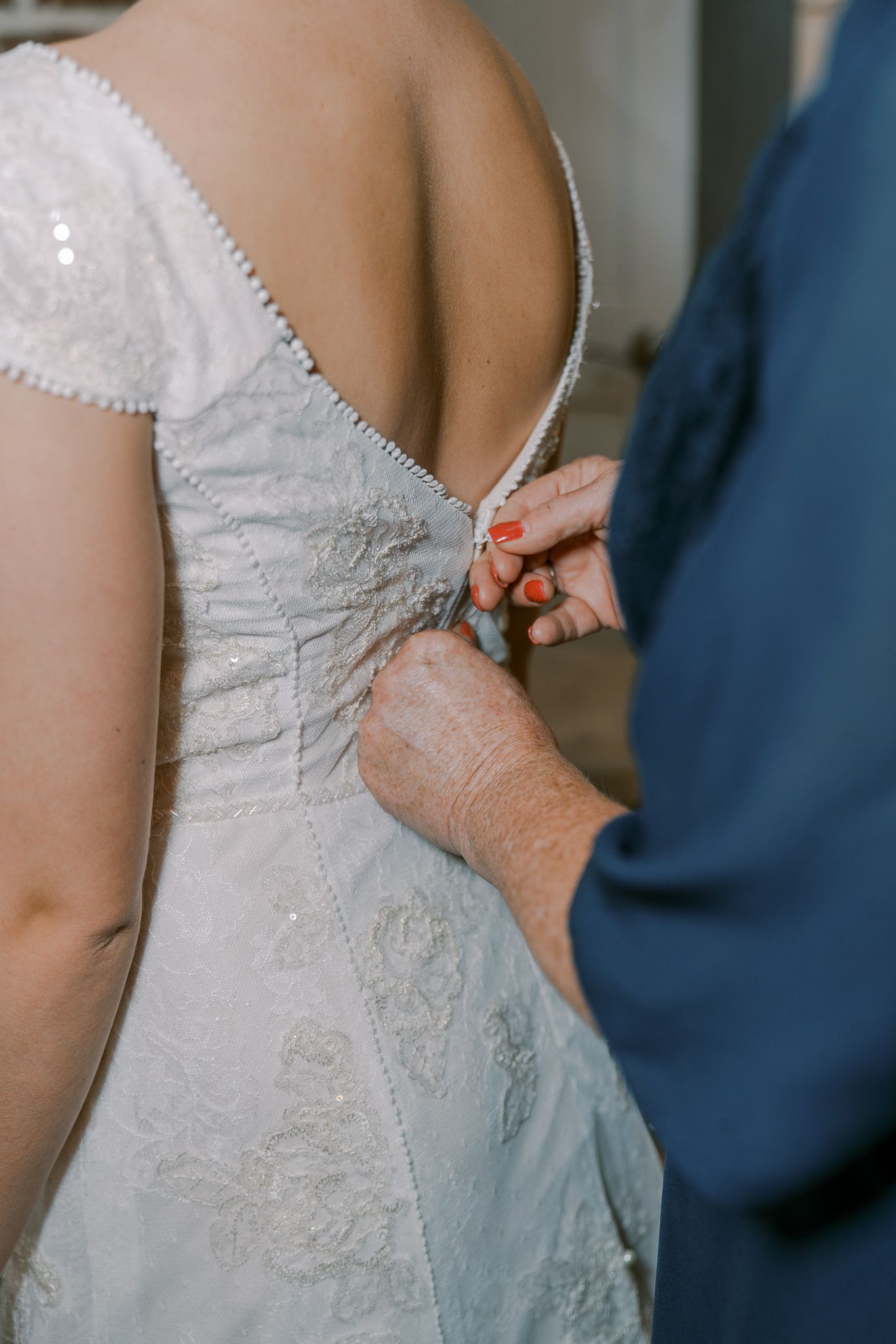 Close-up view of someone helping to button up a delicate white lace wedding dress.
