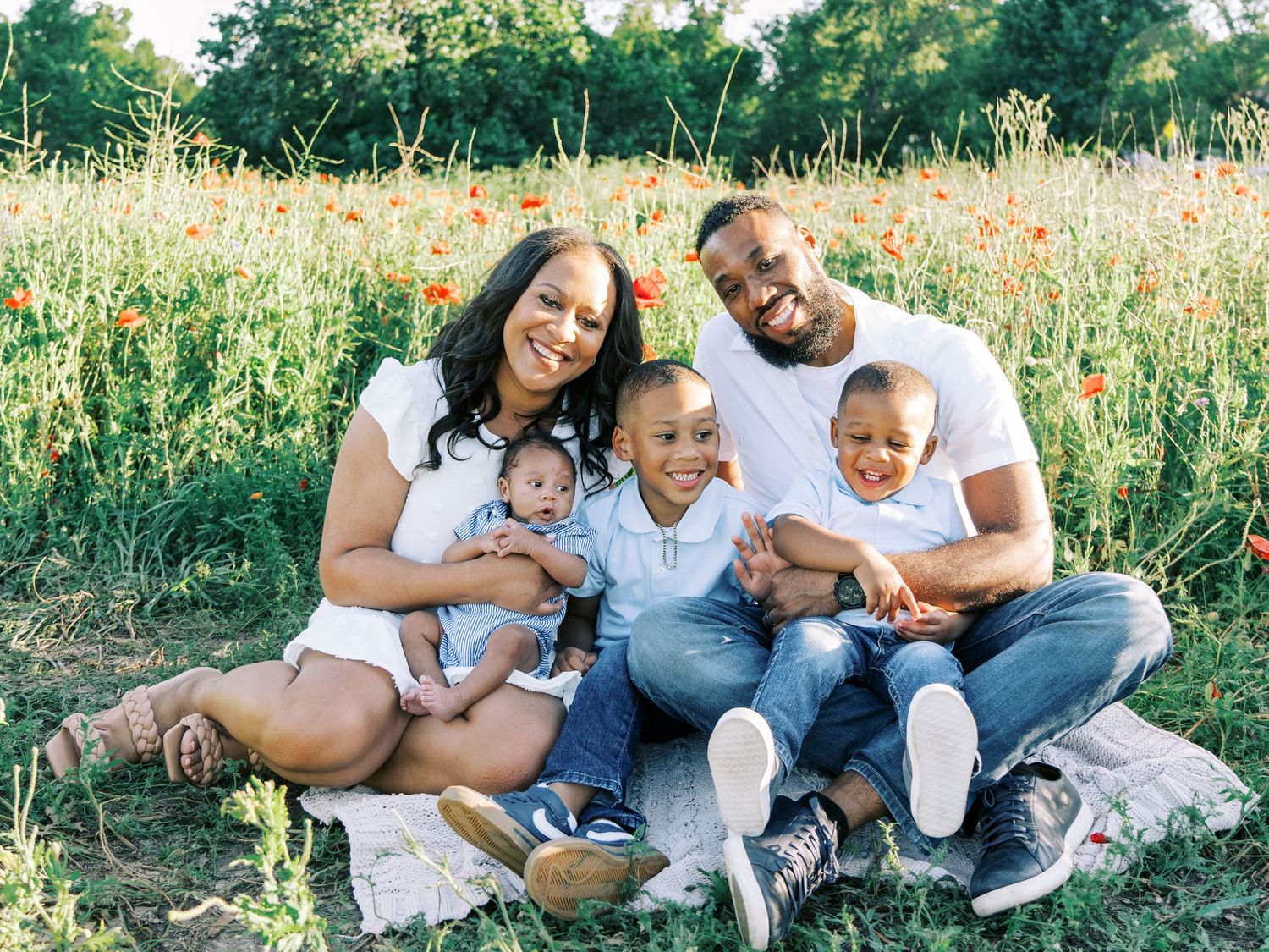 Family wearing white sits together in a wildflower meadow during golden hour sunset photo session.