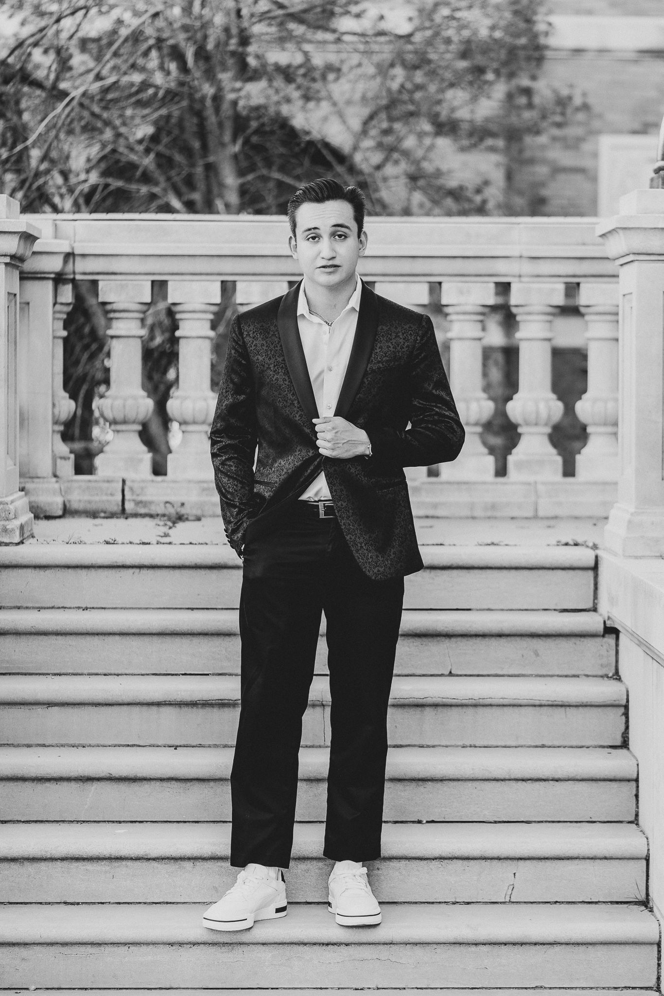 A black and white photo of someone in formal attire and casual shoes sitting on ornate stone steps.